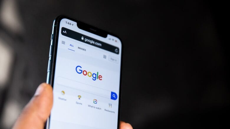 A hand holds a smartphone displaying the Google search homepage on its screen.