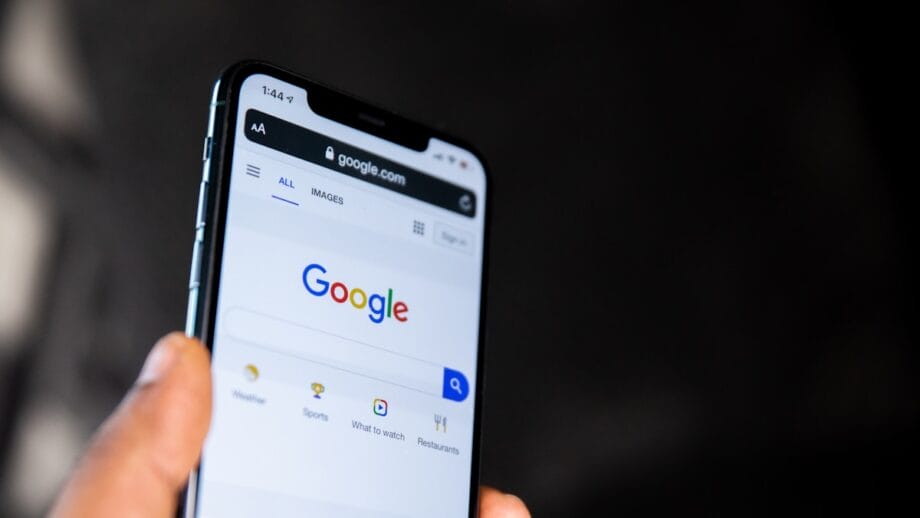 A hand holds a smartphone displaying the Google search homepage on its screen.