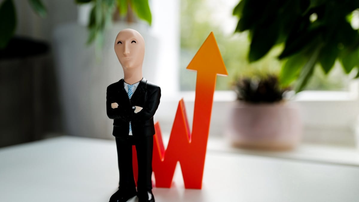 A figurine of a person in a suit stands in front of an orange upward arrow symbol, suggesting growth or success.
