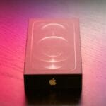 A sealed iPhone box sits on a wooden surface with colorful lighting.