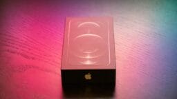 A sealed iPhone box sits on a wooden surface with colorful lighting.