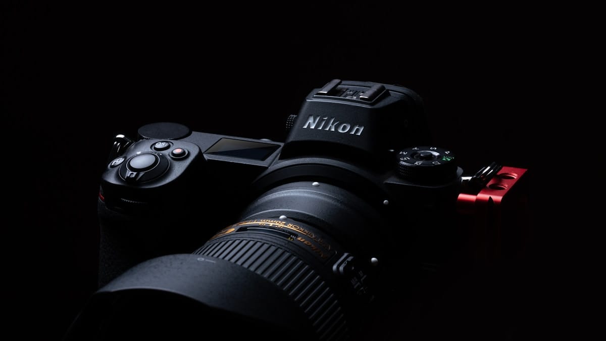 A close-up of a Nikon DSLR camera with a lens attached, photographed against a dark background.