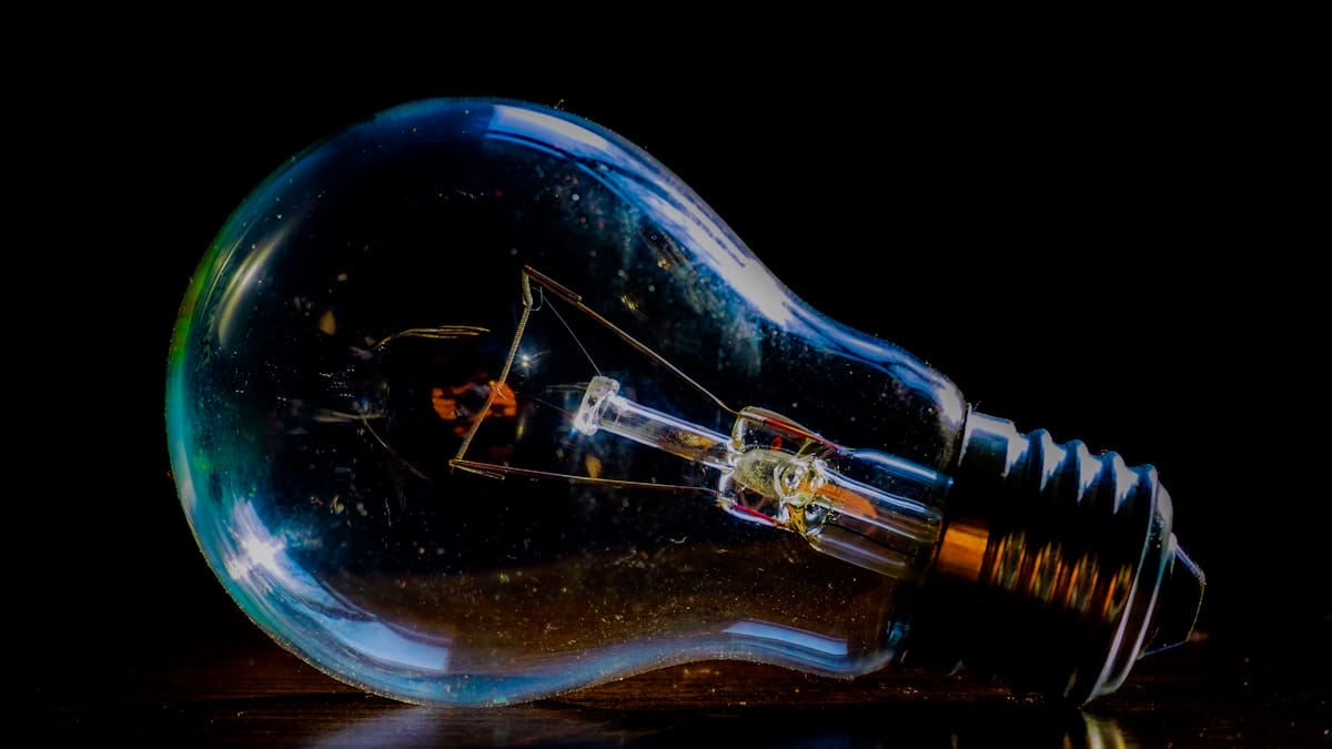 A clear incandescent light bulb lies on its side against a dark background, highlighting its filament and metal base.