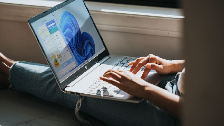 Person using a laptop with a Windows 11 interface, sitting by a window in natural light.