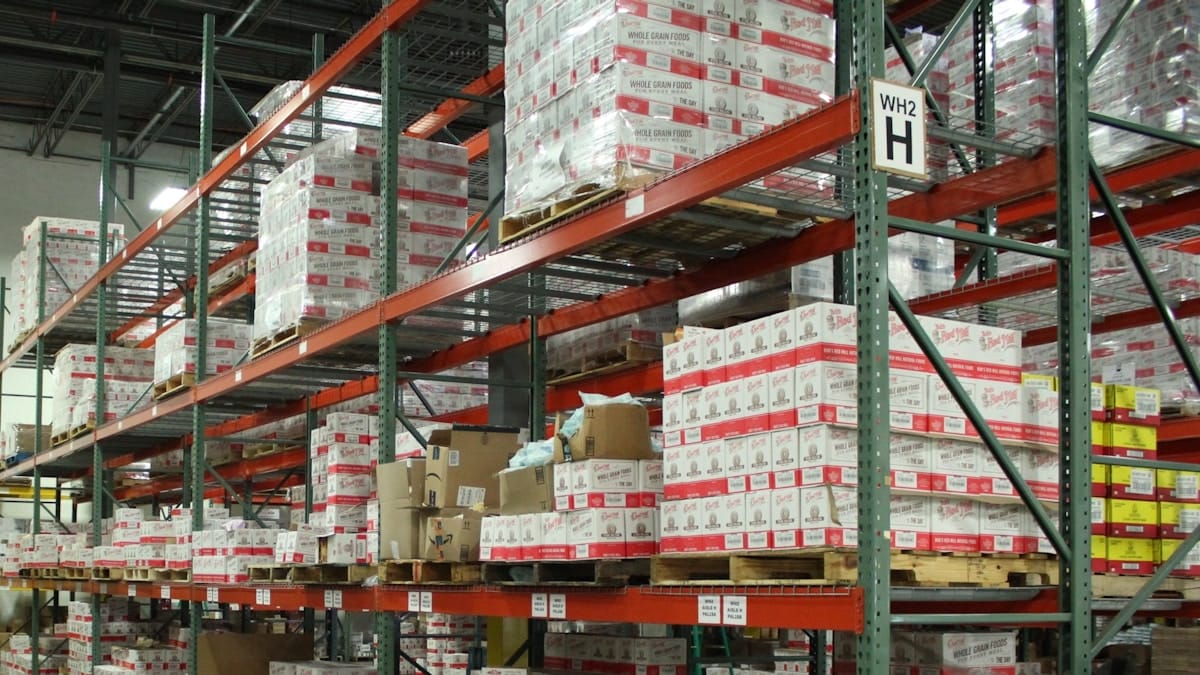 Warehouse shelves filled with stacked boxes and packages, some on pallets, in an industrial storage area.