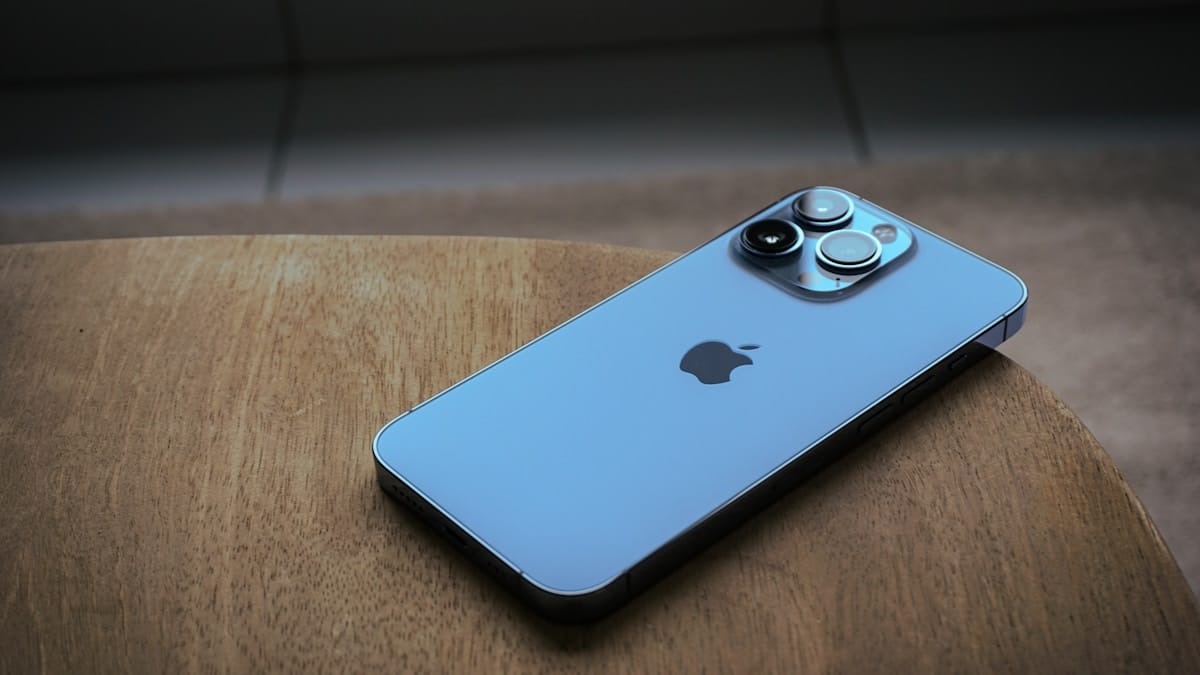 A silver iPhone with three rear cameras placed face down on a wooden surface.
