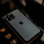 A silver iPhone placed face down on its box, showing the Apple logo and three camera lenses.