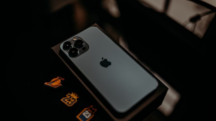 A silver iPhone placed face down on its box, showing the Apple logo and three camera lenses.