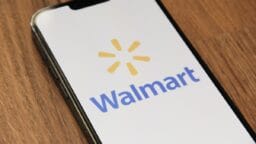 A smartphone displays the Walmart logo on its screen while resting on a wooden surface.