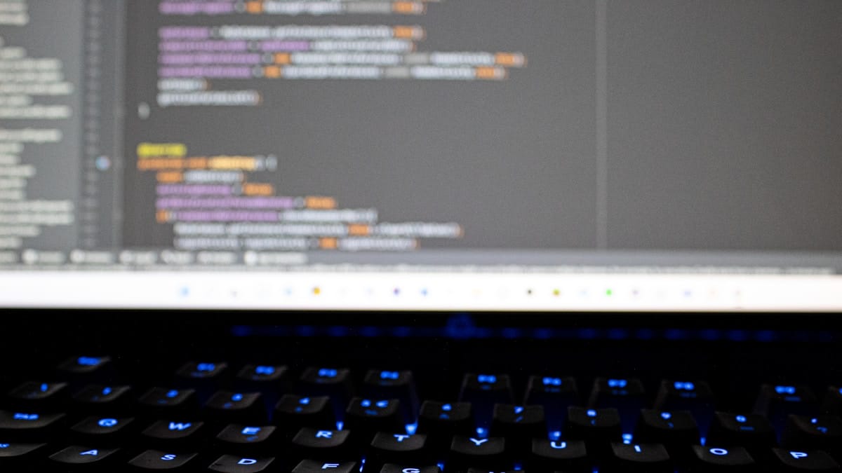 A computer screen displays lines of code above a backlit keyboard with blue illuminated keys.