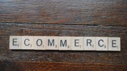 Scrabble tiles spelling ECOMMERCE are arranged in a row on a dark wooden surface.