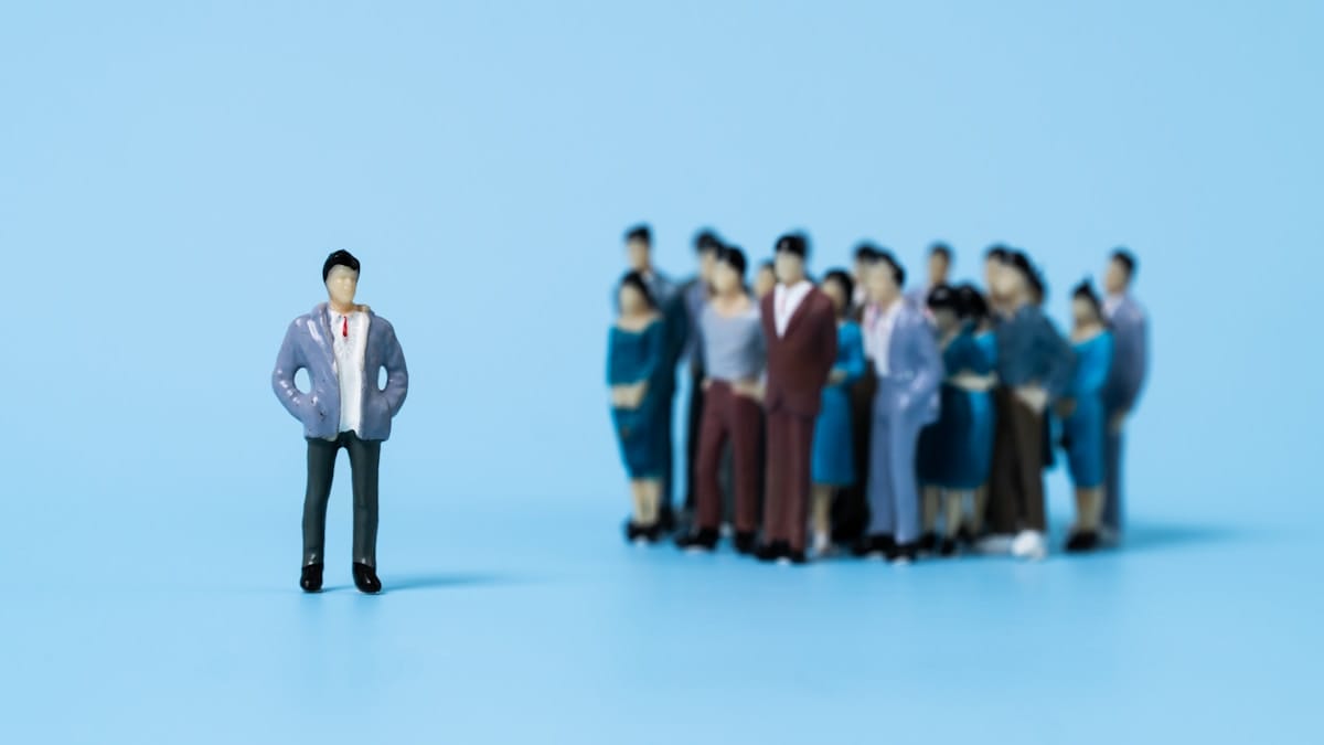 A single figurine stands apart from a group of figurines on a blue background.