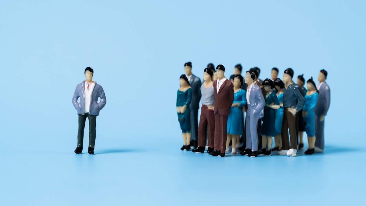 A group of miniature figurines stands together while a single figurine stands alone against a blue background.
