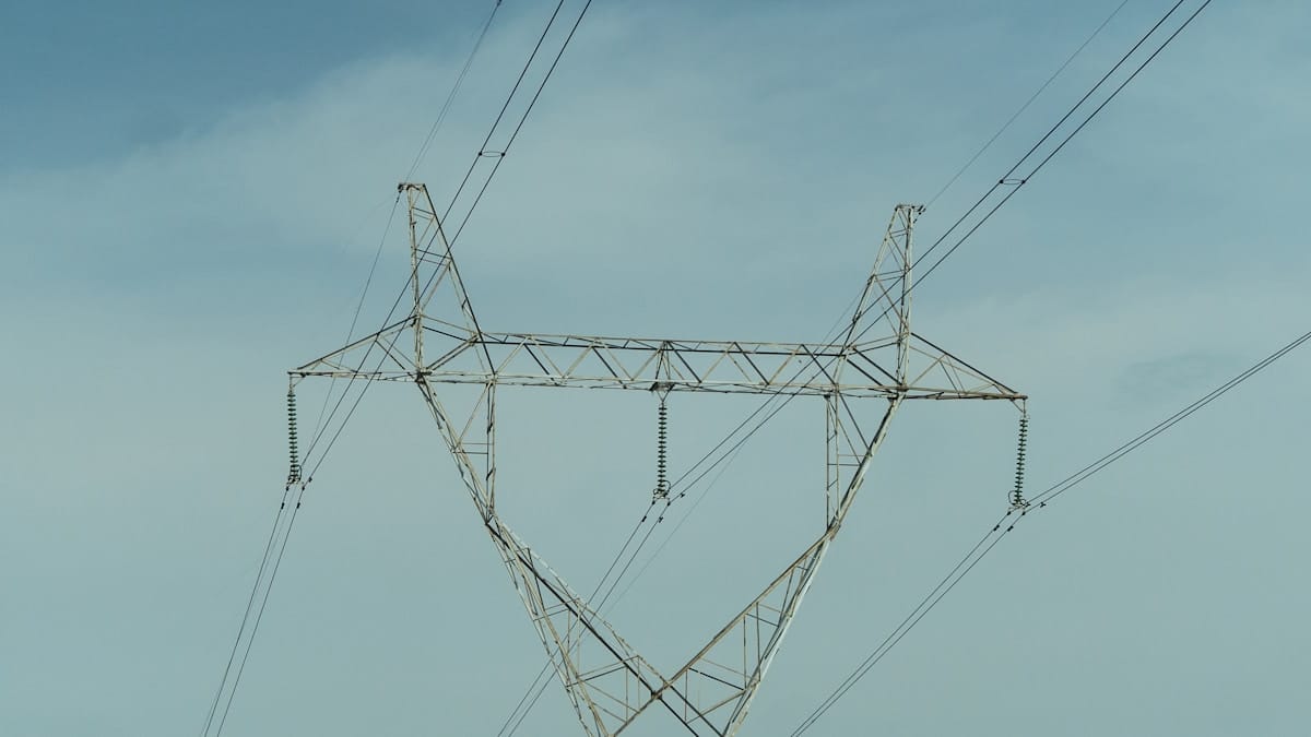 A metal electrical transmission tower with multiple power lines set against a clear blue sky.