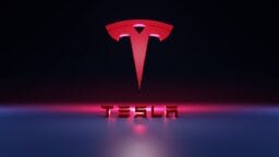 Red Tesla logo above the word TESLA in bold 3D letters, set against a dark background with pink and blue lighting effects.