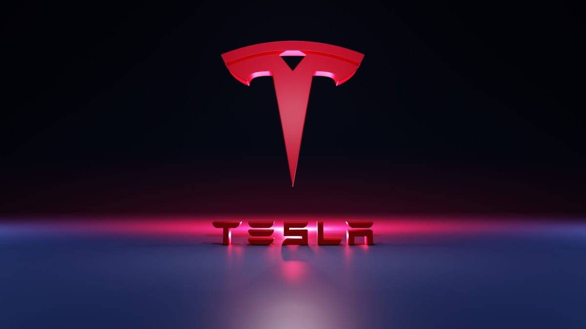 Red Tesla logo above the word TESLA in bold 3D letters, set against a dark background with pink and blue lighting effects.