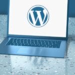 A laptop on a speckled surface displays the WordPress logo on its screen.