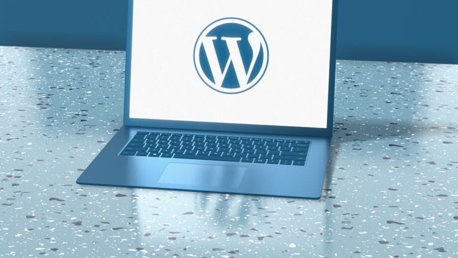 A laptop on a speckled surface displays the WordPress logo on its screen.