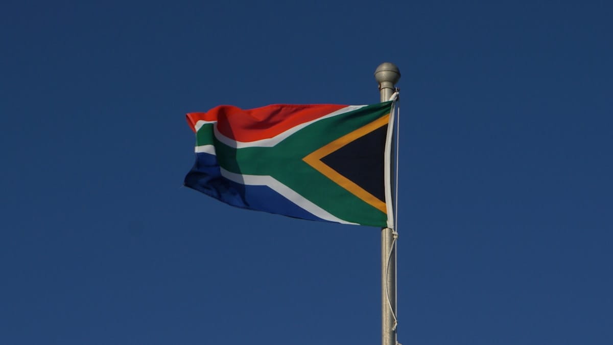 The national flag of South Africa flies on a flagpole against a clear blue sky.