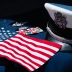U.S. flag, military medals, insignia, and a white service cap displayed on a dark fabric background.