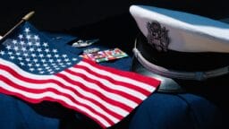 U.S. flag, military medals, insignia, and a white service cap displayed on a dark fabric background.