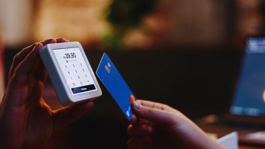 A person holds a blue credit card near a card reader displaying a payment amount of 39.90 for contactless payment.