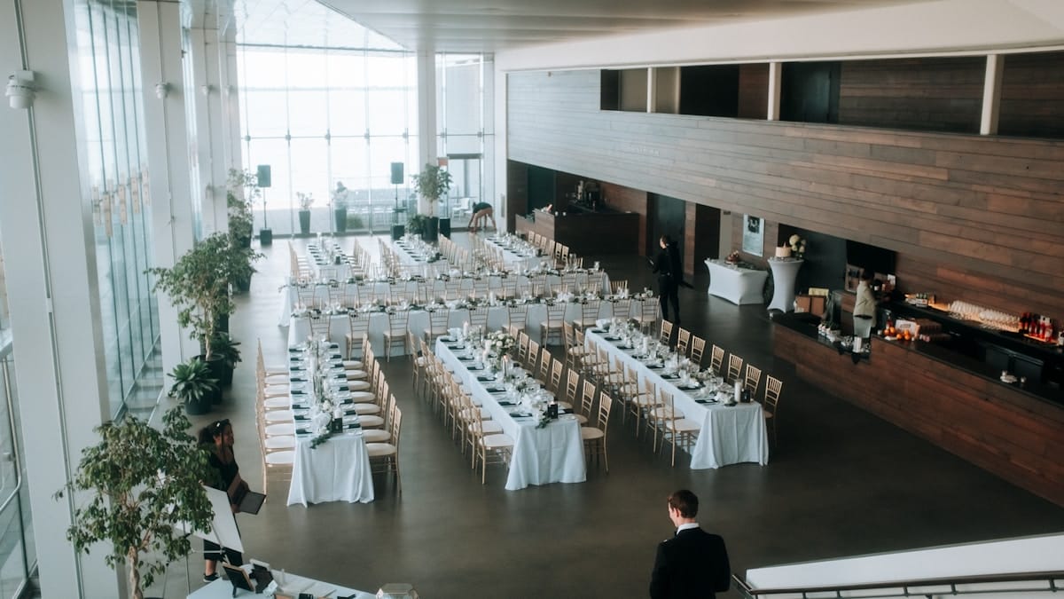 Spacious, modern event hall set up with long banquet tables and chairs, decorated for a formal gathering or reception.