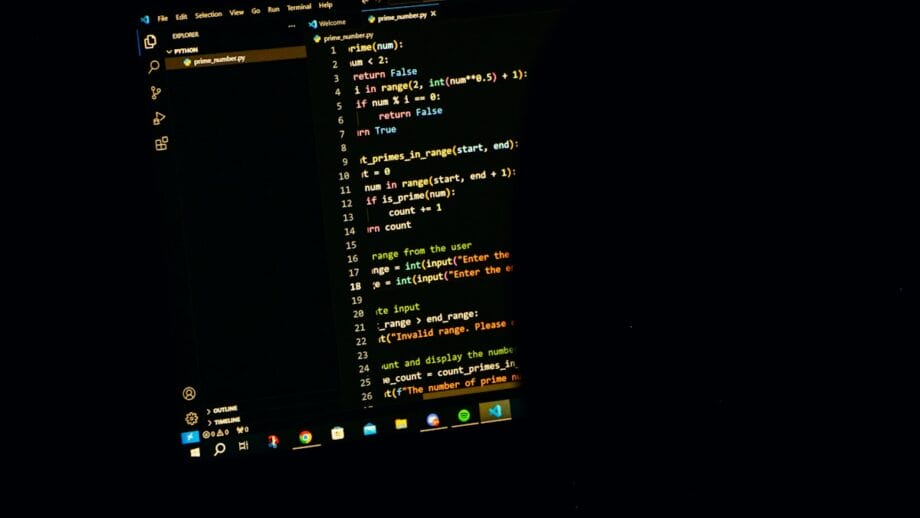 A computer screen displays Python code in a dark-themed text editor, showing a function to find prime numbers in a range.