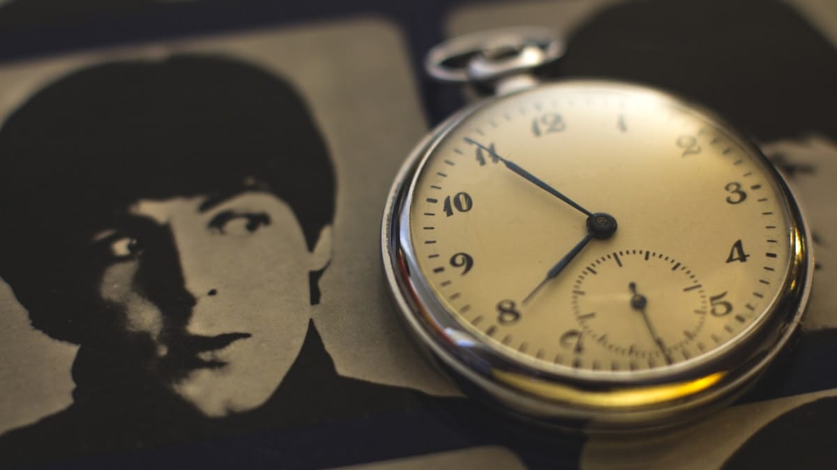 A pocket watch lies on top of a black-and-white photograph of a persons face.