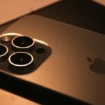 Close-up of the back of an iPhone showing three camera lenses and the Apple logo on a dark surface.