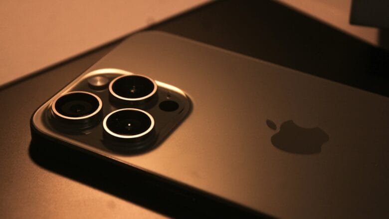 Close-up of the back of an iPhone showing three camera lenses and the Apple logo on a dark surface.
