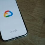 A smartphone displaying the Google Cloud logo on its screen rests on a wooden surface next to a notebook.