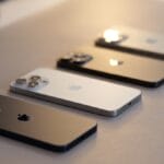 Four iPhones in different colors are placed face down in a row on a light-colored surface.