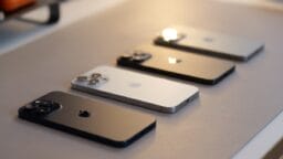 Four iPhones in different colors are placed face down in a row on a light-colored surface.