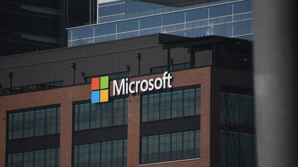The Microsoft logo is displayed on the exterior of a modern, multi-story office building.