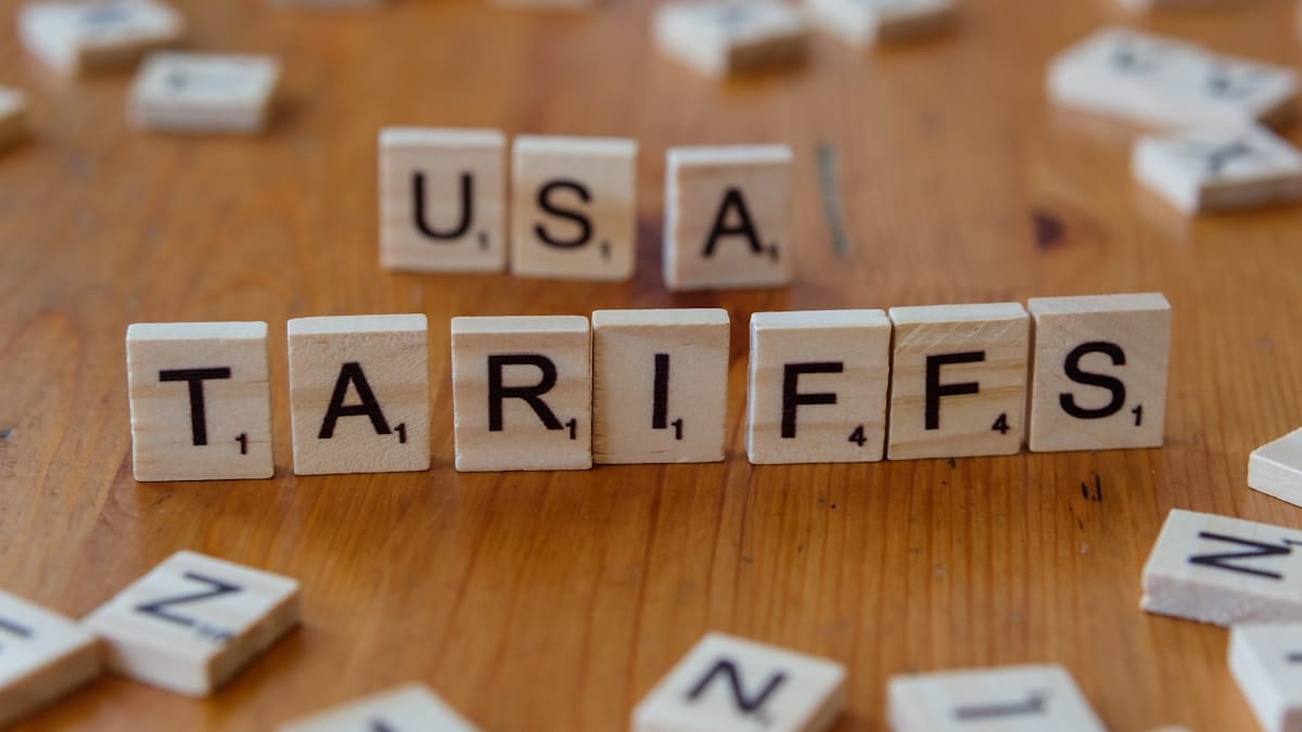 Wooden letter tiles on a table spell out USA and TARIFFS, with other scattered tiles in the background.