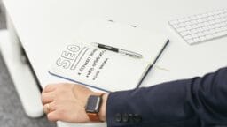 Open notebook on a desk with SEO written, listing keyword research, web optimization, and link building; a pen rests on the page.