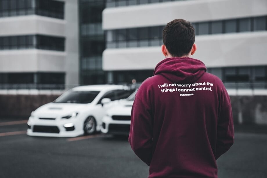 a man in a maroon hoodie standing in front of a white car