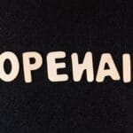 Wooden letters spelling OPENAI are arranged on a textured black surface.