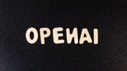 Wooden letters spelling OPENAI are arranged on a textured black surface.