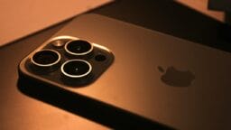 Close-up of the back of an iPhone showing the camera lenses and Apple logo under warm lighting.
