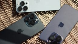 Three iPhones with triple-lens cameras are placed on a woven surface with their backs facing up.