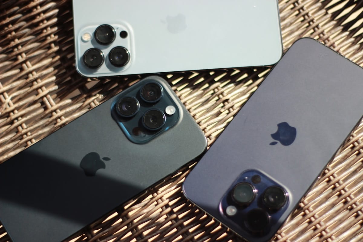 Three iPhones with triple-lens cameras are placed on a woven surface with their backs facing up.