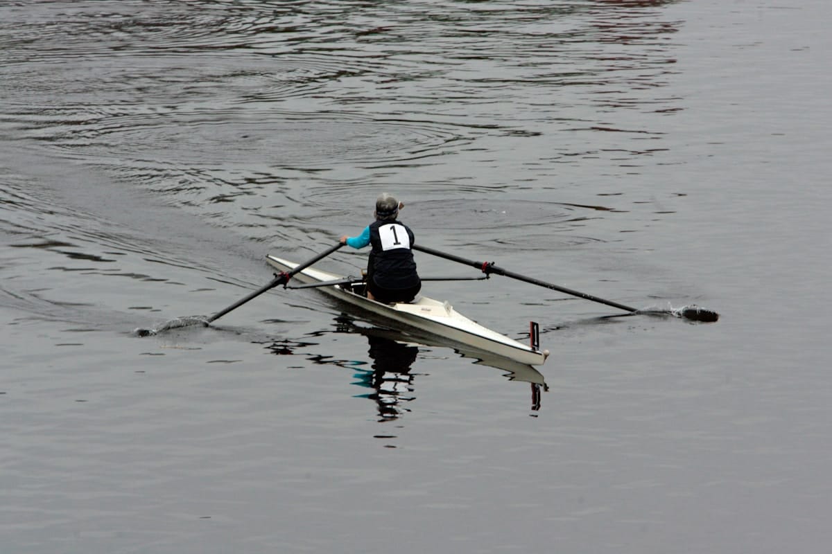 A single rower wearing number 1 rows a scull boat on calm water, creating ripples behind them.