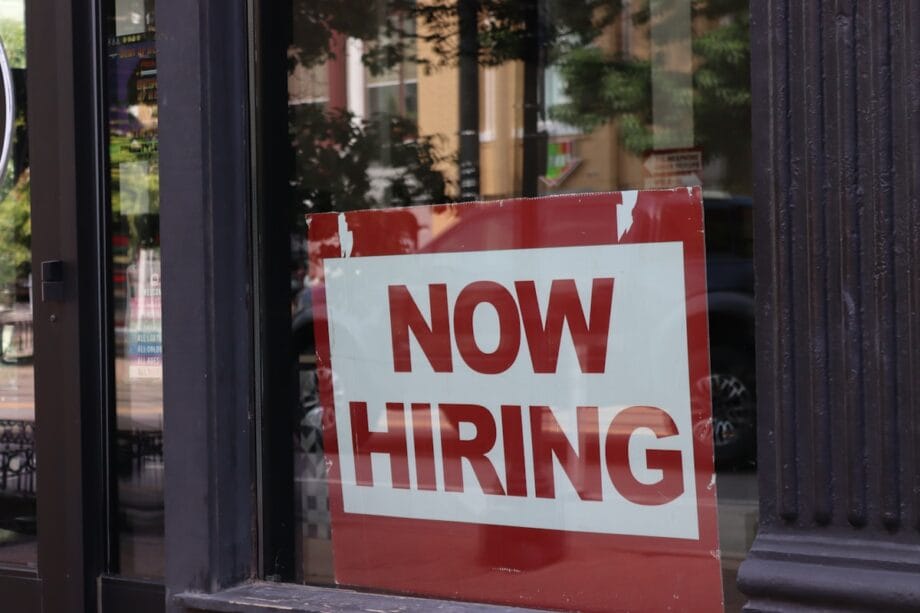 A "now hiring" sign hangs in a store window.