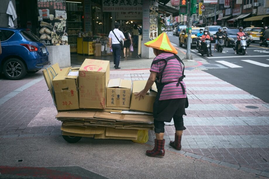 A woman with a yellow cone on her head is pushing a cart full of boxes