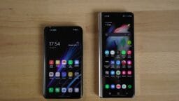 Two smartphones with their home screens on are placed side by side on a light wooden surface.