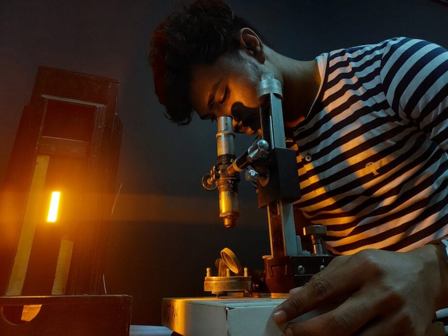A man in striped shirt looking through a microscope