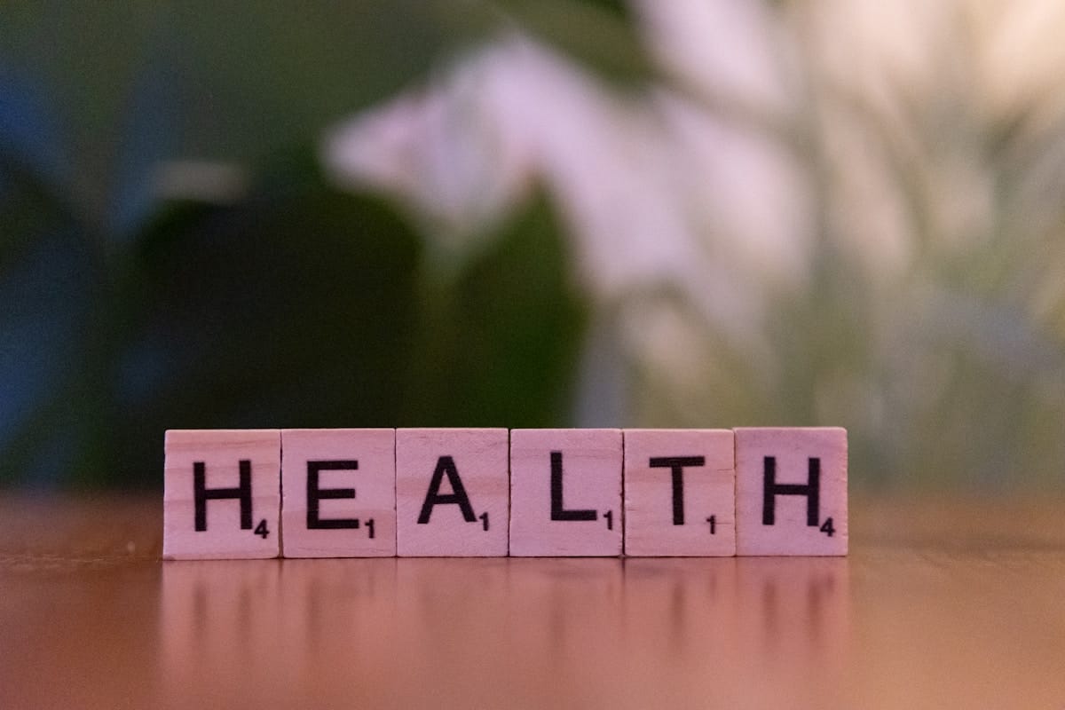 Wooden Scrabble tiles on a table spell out the word HEALTH with a blurred green background.