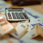 A calculator and several euro banknotes placed on financial documents with graphs and charts.